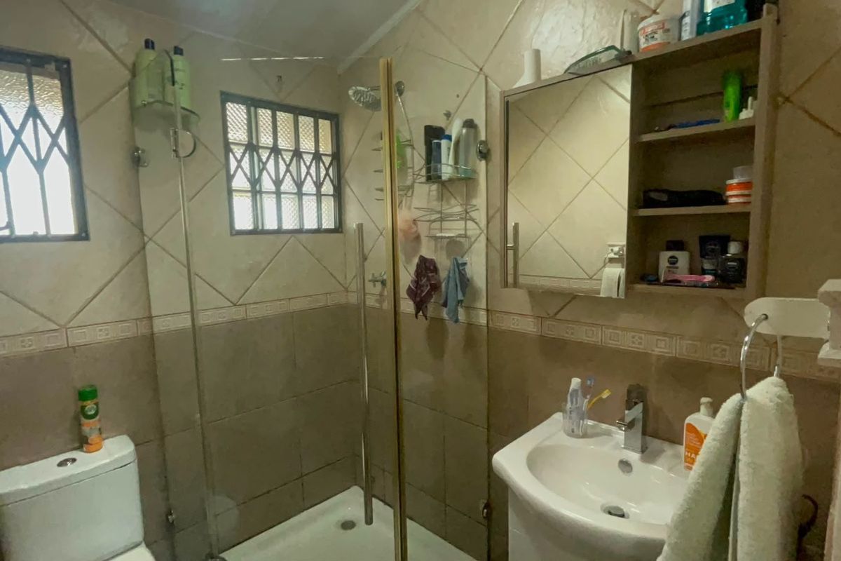 A functional bathroom featuring a shower enclosure, vanity basin, toilet, and built-in medicine cabinet with tiled wall finishes.