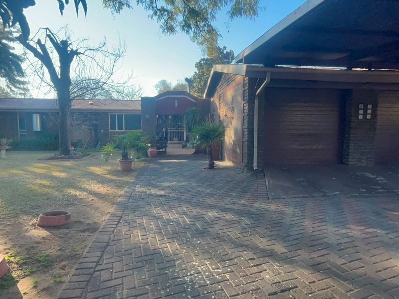 Front view of the property featuring a brick driveway, double garage, covered carport, and established garden area.