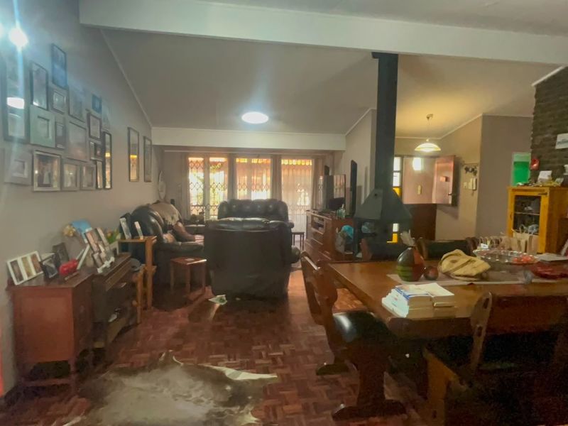 Spacious open-plan living and dining area featuring classic parquet flooring, an exposed brick feature wall, and a central freestanding fireplace.