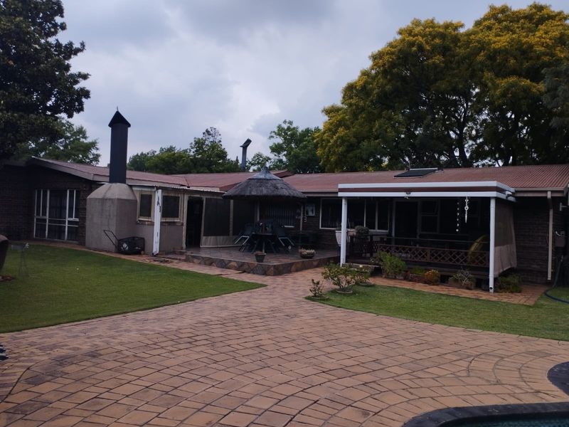 Rear exterior view featuring a paved courtyard, covered patio area, outdoor fireplace, and a thatched lapa set against the back of the house.