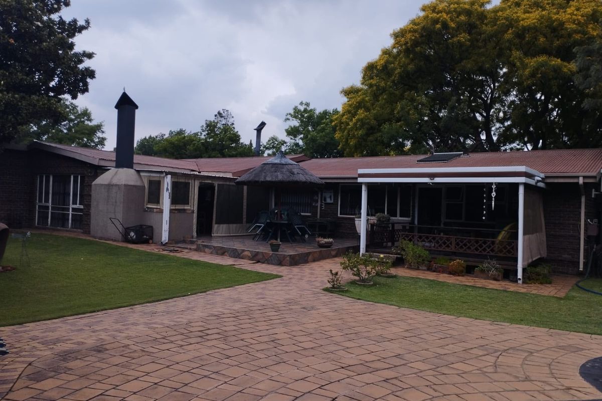Rear exterior view featuring a paved courtyard, covered patio area, outdoor fireplace, and a thatched lapa set against the back of the house.