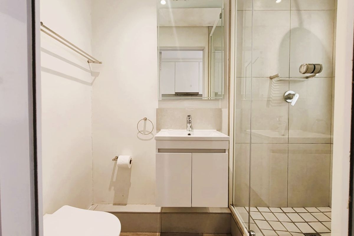 A modern bathroom featuring a vanity cabinet with basin, a wall-mounted mirror, and a glass-enclosed shower with tiled flooring.