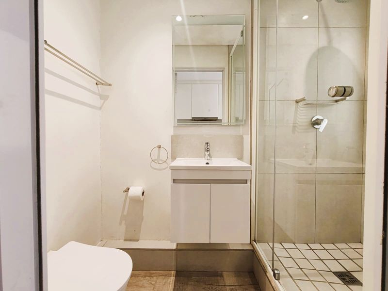 A modern bathroom featuring a vanity cabinet with basin, a wall-mounted mirror, and a glass-enclosed shower with tiled flooring.