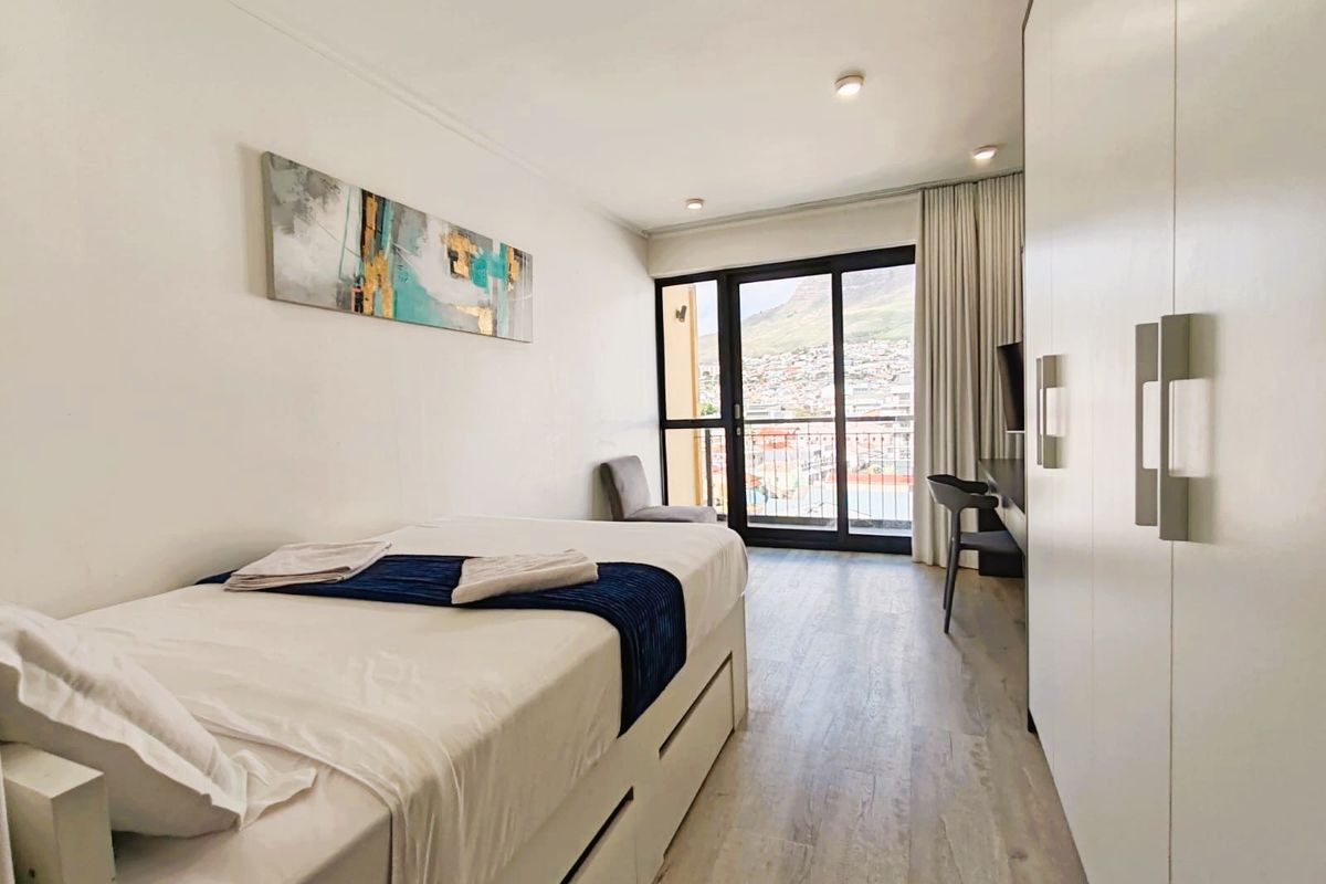 A bright bedroom featuring built-in wardrobes, laminate flooring, and a sliding glass door leading to a balcony with scenic views.