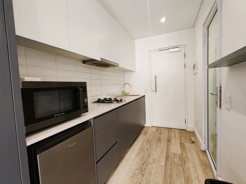 Modern galley-style kitchen featuring sleek grey and white cabinetry, stone countertops, gas hob, extractor fan, and durable laminate flooring.