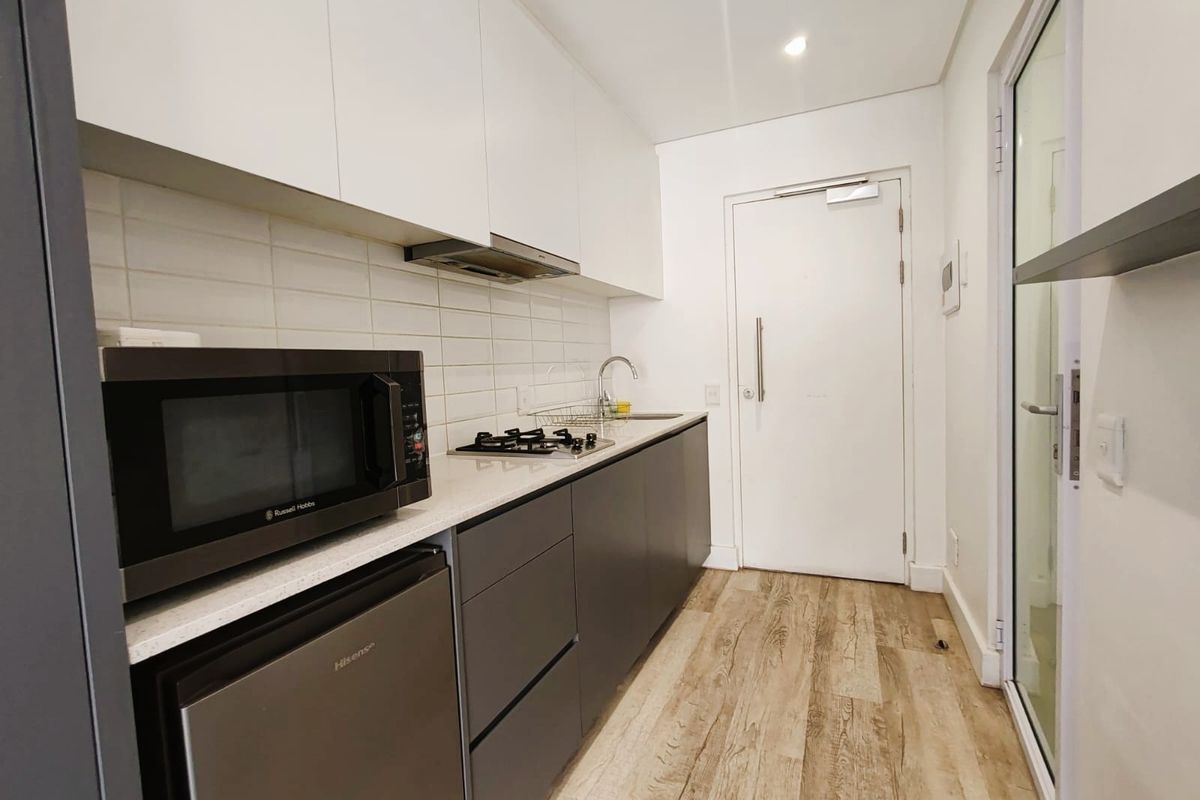 Modern galley-style kitchen featuring sleek grey and white cabinetry, stone countertops, gas hob, extractor fan, and durable laminate flooring.