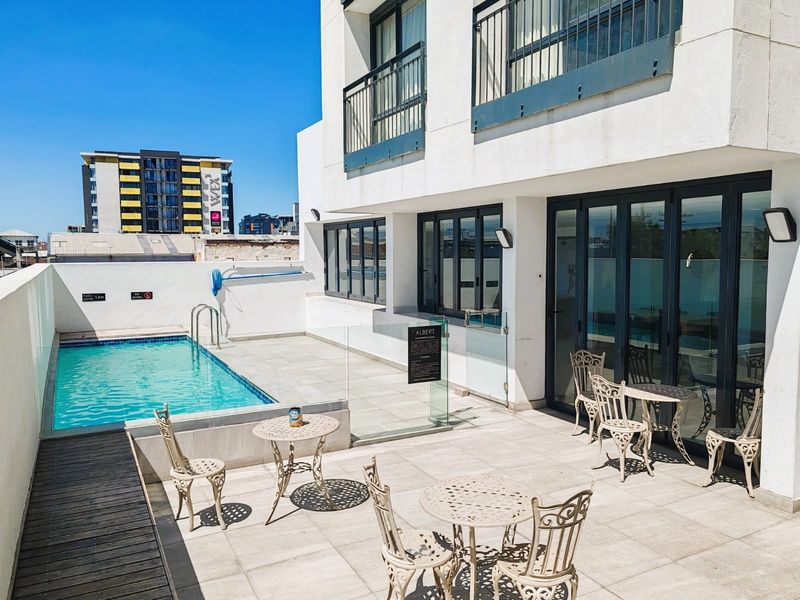 A well-maintained outdoor pool area featuring a tiled patio, glass balustrades, and direct access to the apartment via bi-fold doors.