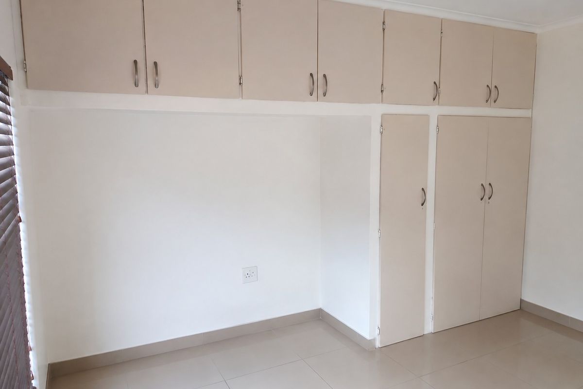 A clean, empty bedroom featuring neutral-toned built-in cupboards and tiled flooring, providing a versatile space ready for personalization.