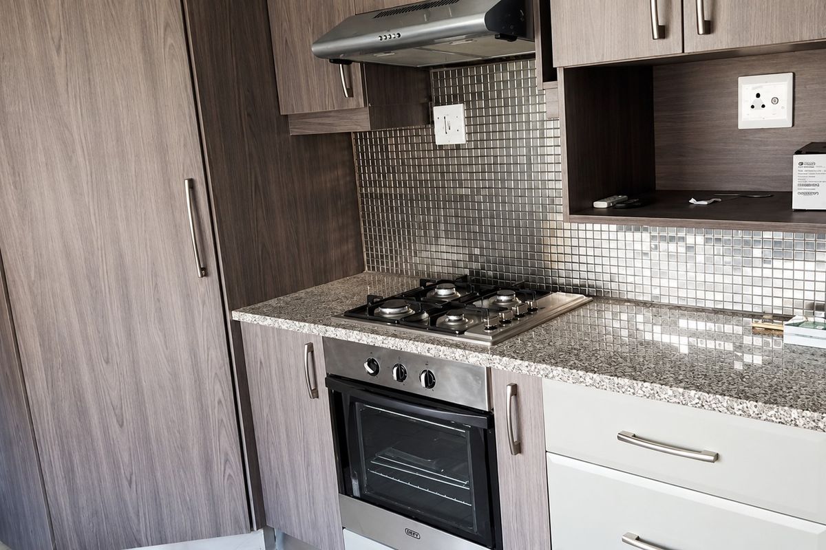 Modern kitchen featuring wood-grain cabinetry, granite countertops, a gas hob, built-in oven, extractor fan, and a stylish mosaic tile backsplash.