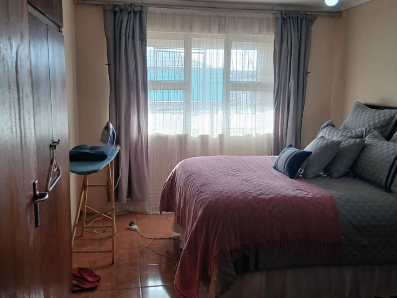 A functional bedroom featuring tiled flooring, a built-in wardrobe, and natural light through an aluminium-framed window.