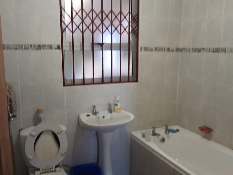 A functional bathroom featuring a pedestal washbasin, bathtub, and toilet, finished with tiled walls and a security gate on the window.