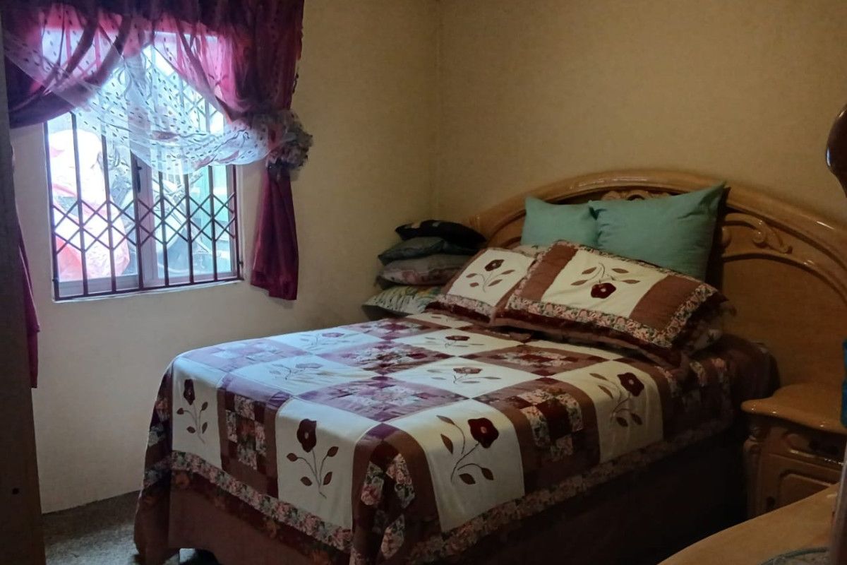 A bedroom featuring security bars on the window and dated interior finishes, offering a functional space with potential for modernization.