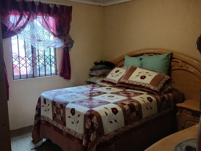 A bedroom featuring security bars on the window and dated interior finishes, offering a functional space with potential for modernization.