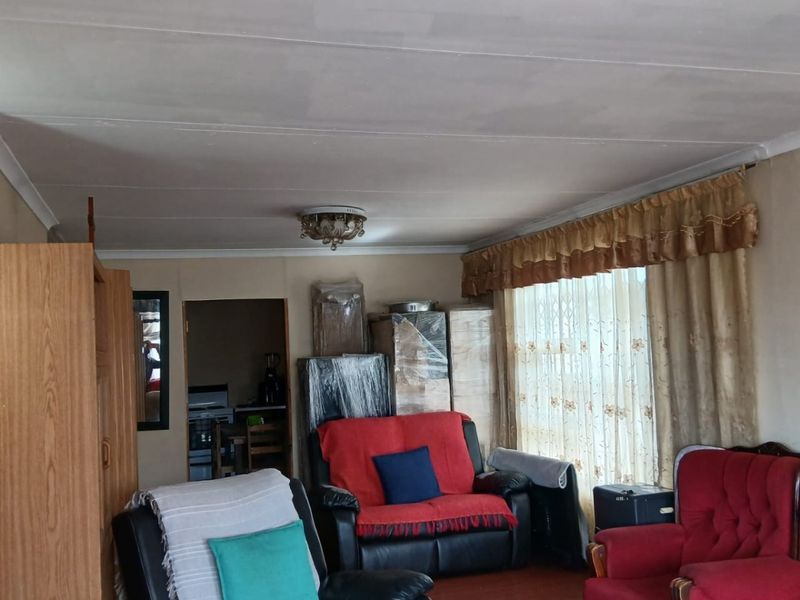 A living room featuring laminate flooring and ceiling-mounted light fixtures, with visible ceiling panel joints requiring cosmetic attention.