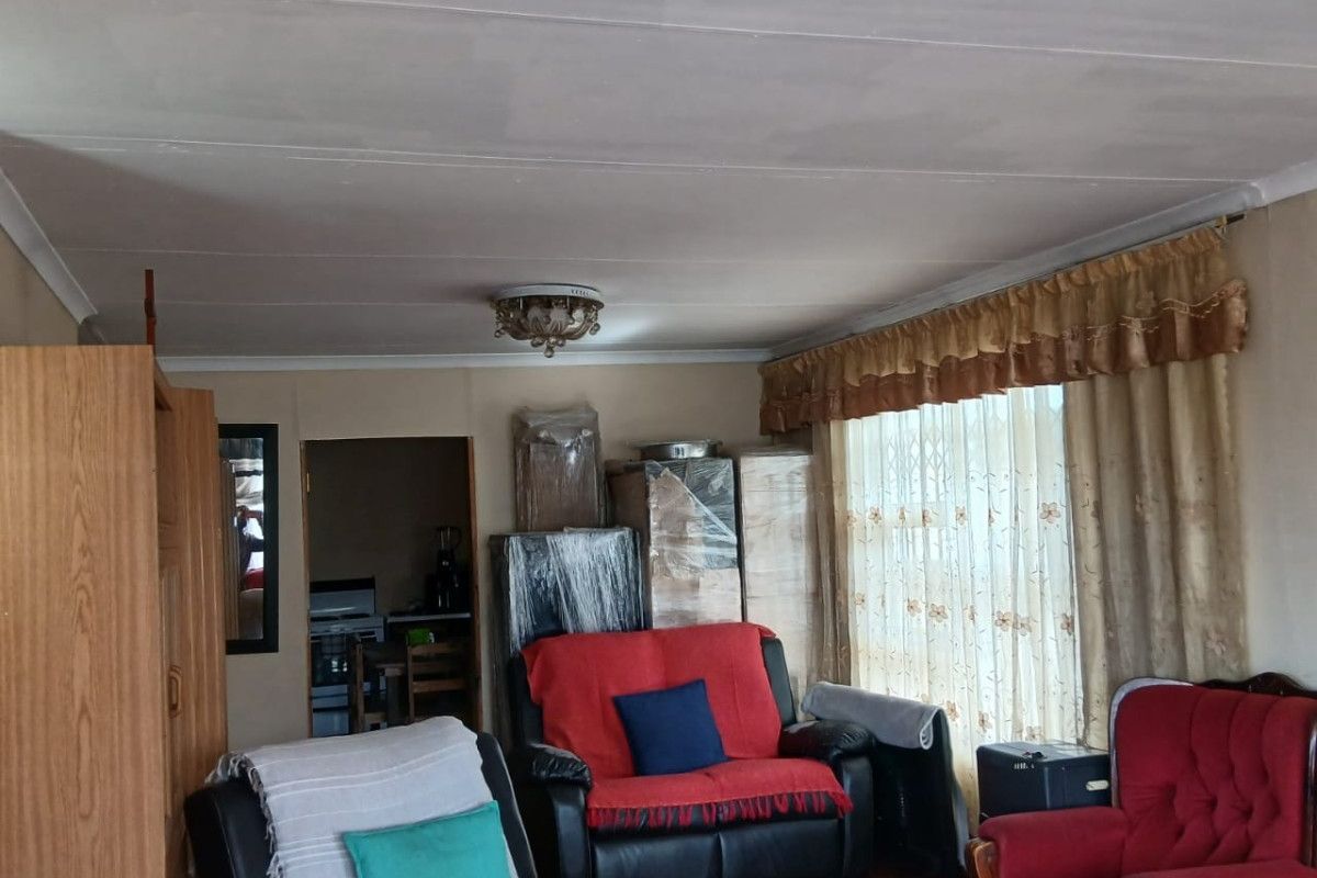 A living room featuring laminate flooring and ceiling-mounted light fixtures, with visible ceiling panel joints requiring cosmetic attention.
