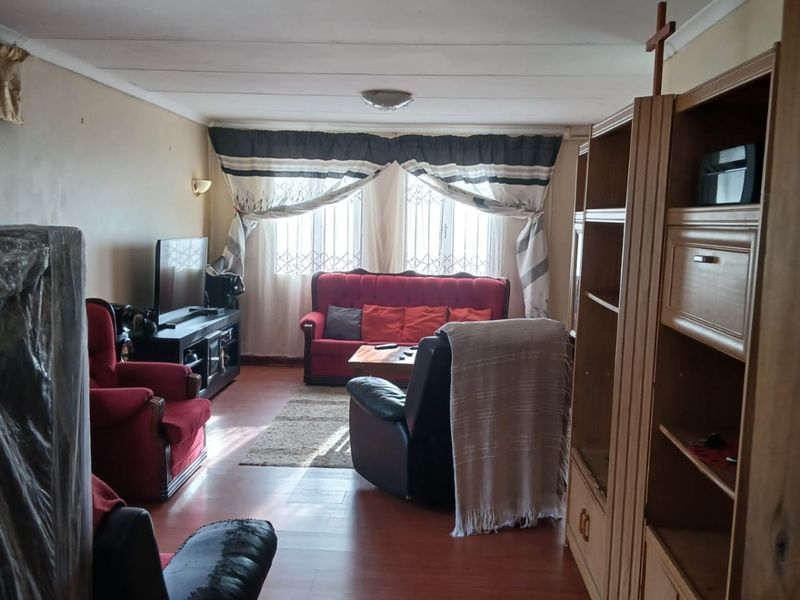 A living room featuring laminate flooring, window security bars, and a central ceiling light fixture, presenting an opportunity for cosmetic updates.