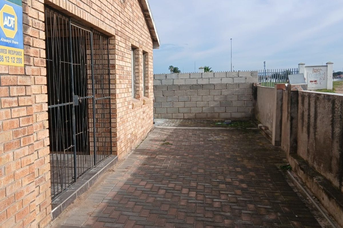 A side view of the property featuring a face brick exterior, paved patio area, and a secure boundary wall with some surface staining.