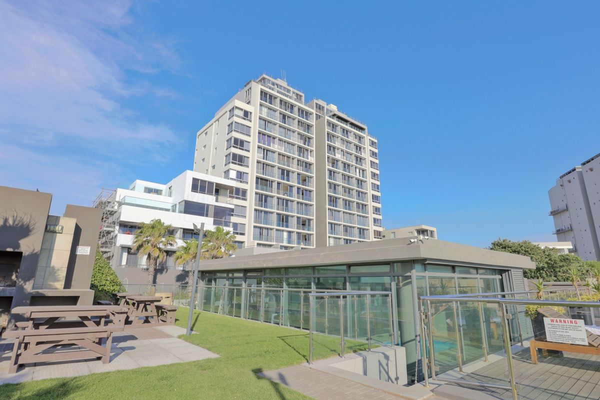 View of a modern multi-story apartment complex featuring a landscaped lawn, paved patio area, and a glass-enclosed pool facility.