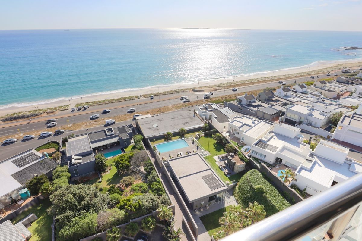 An elevated aerial view showcasing the coastal neighborhood, beachfront, and surrounding residential properties with private swimming pools and solar installations.