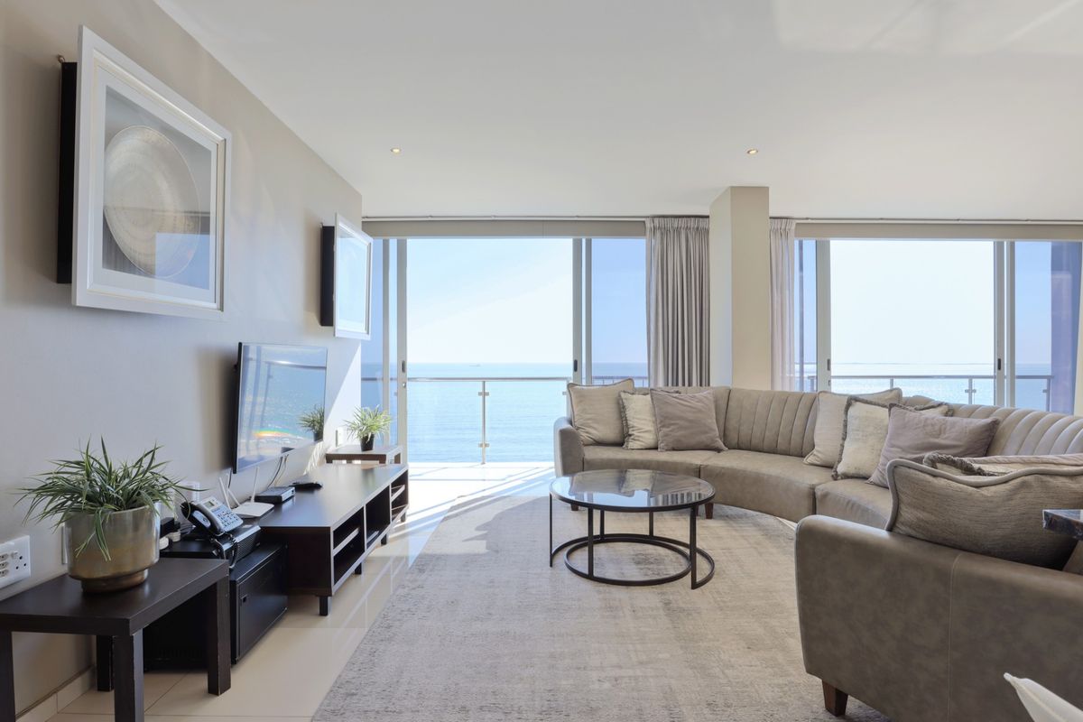 Spacious living room featuring large sliding glass doors that open to a balcony with expansive ocean views and modern tiled flooring.