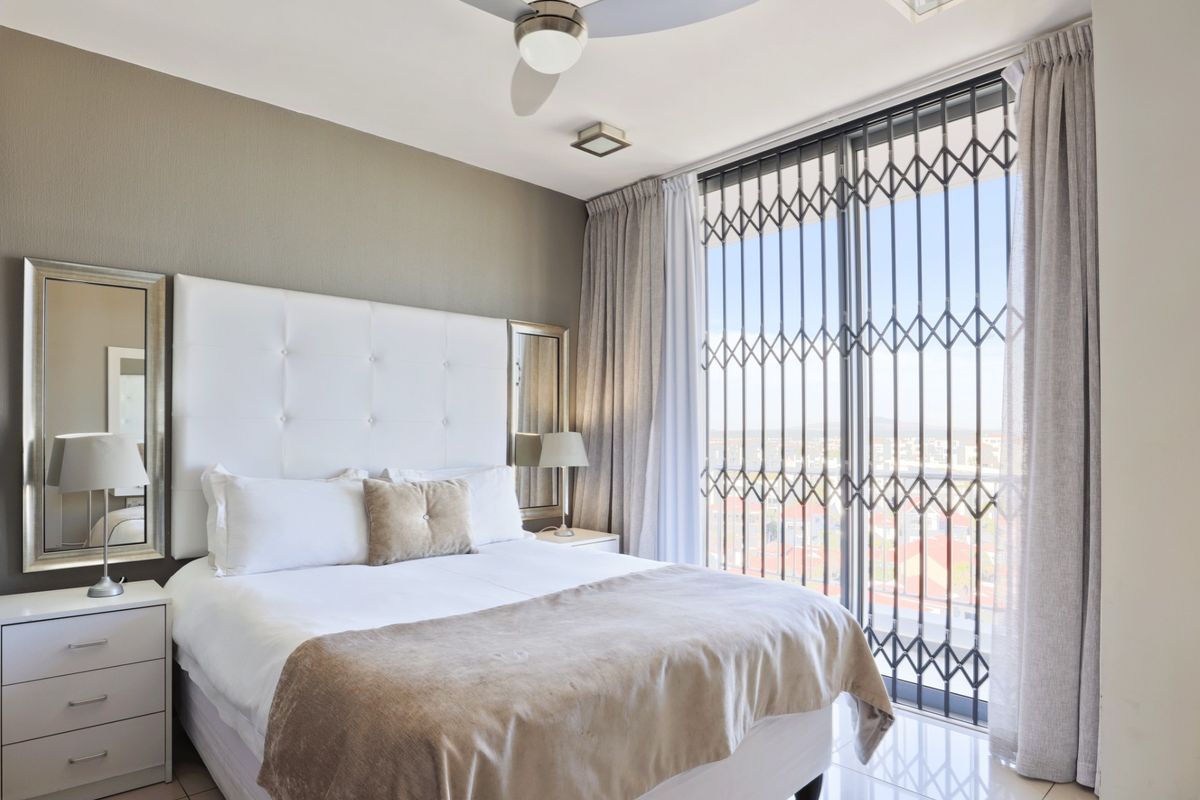 A well-maintained bedroom featuring tiled flooring, a ceiling fan, and a sliding glass door with a security gate leading to an exterior view.