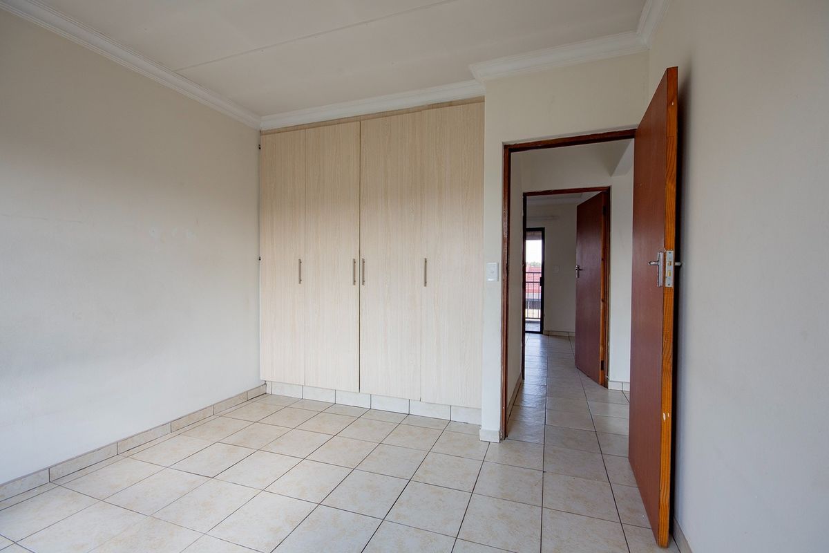 An empty bedroom featuring light-toned built-in cupboards, tiled flooring, and neutral wall finishes, providing a clean and versatile space.