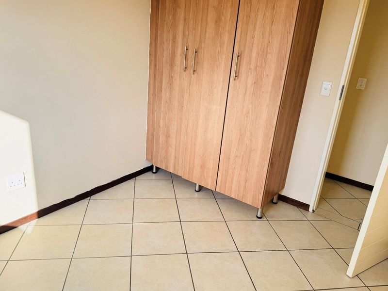 A clean bedroom space featuring neutral tiled flooring and a functional built-in wooden wardrobe.