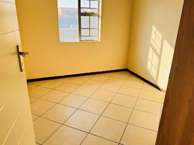 A vacant bedroom featuring neutral tiled flooring, a window with security bars, and simple wall finishes, ready for personalization.