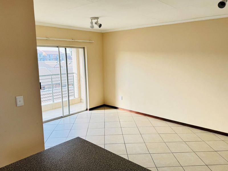 An empty open-plan living area featuring tiled flooring, neutral walls, and a sliding glass door providing access to an outdoor balcony.