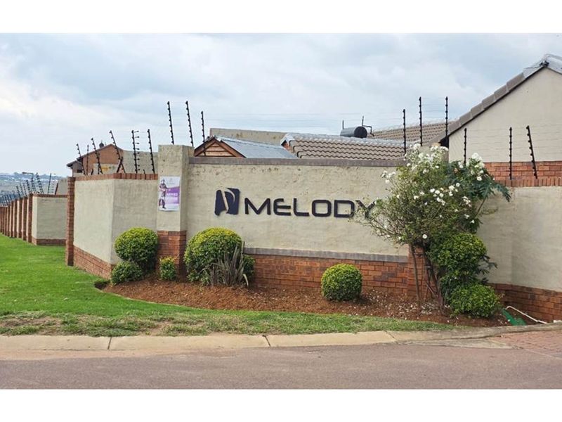 The entrance to Melody complex featuring a secure perimeter wall with electric fencing and prominent signage.