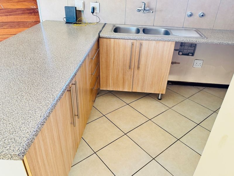 A functional kitchen area featuring laminate cabinetry, a double bowl stainless steel sink, and tiled flooring, ready for minor cosmetic updates.