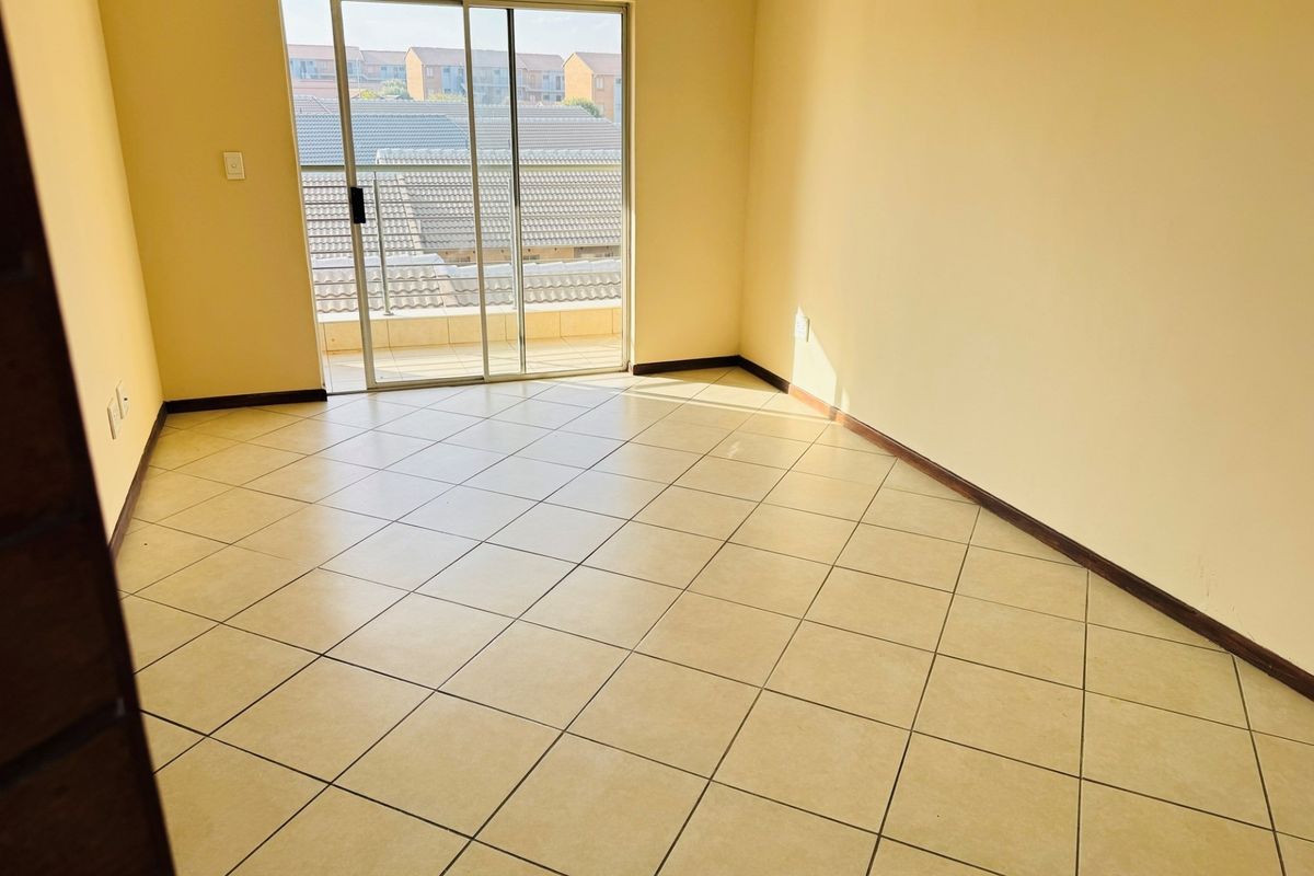An empty bedroom featuring neutral tiled flooring and a sliding glass door providing access to a balcony.