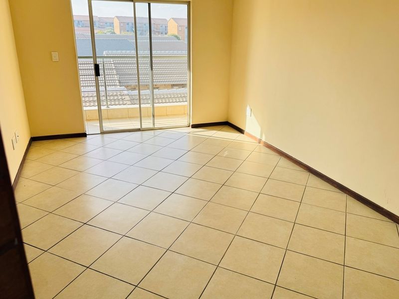 An empty bedroom featuring neutral tiled flooring and a sliding glass door providing access to a balcony.
