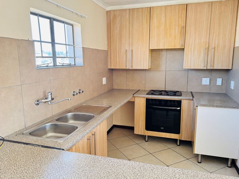 A functional kitchen featuring light wood-look cabinetry, granite-style countertops, a double bowl sink, and a built-in electric oven with hob.