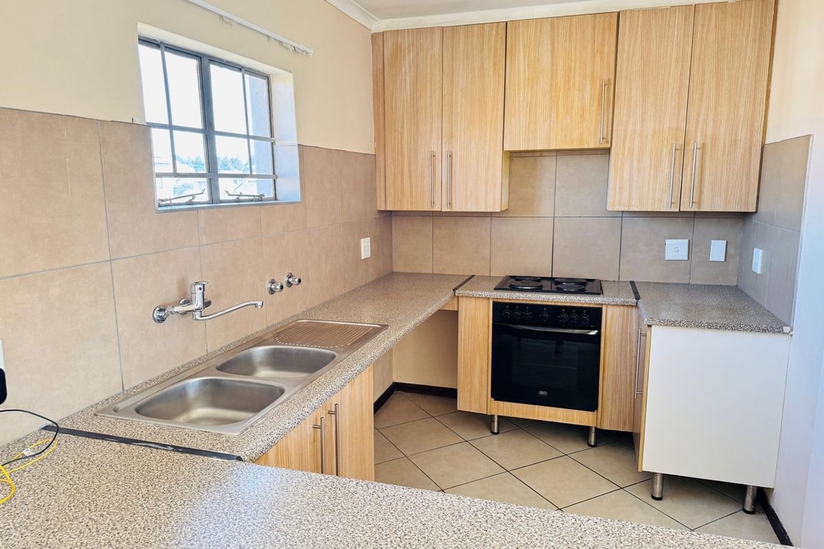 A functional kitchen featuring light wood-look cabinetry, granite-style countertops, a double bowl sink, and a built-in electric oven with hob.