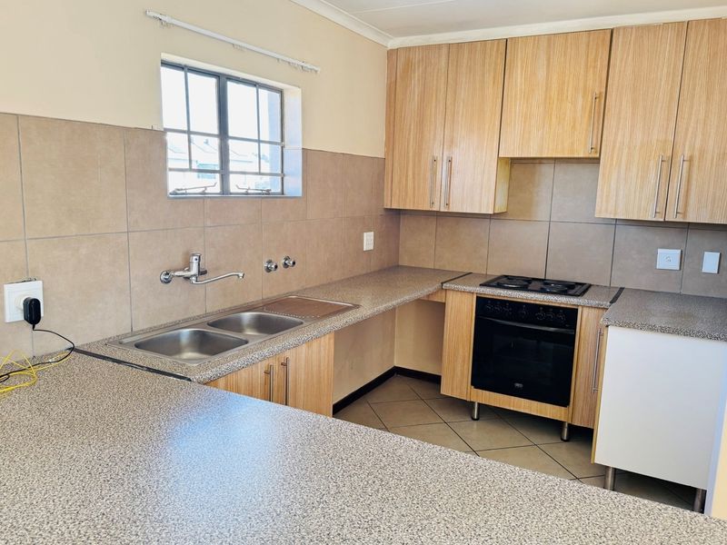A functional kitchen featuring laminate cabinetry, granite-look countertops, a double bowl sink, and a built-in oven with an electric hob.