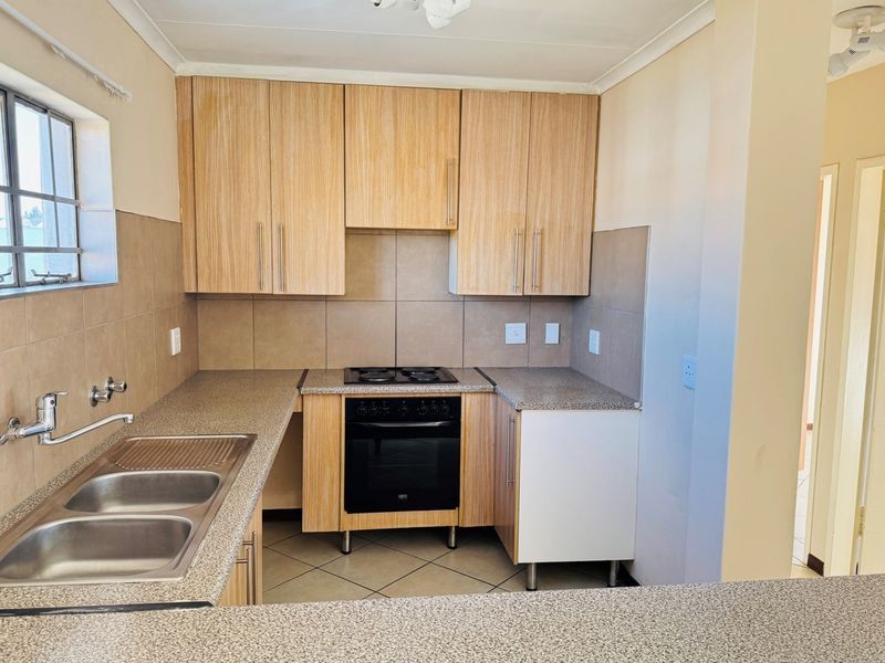 A functional kitchen featuring light wood-finish cabinetry, granite-look countertops, a built-in oven and hob, and a double bowl sink with tiled backsplash.