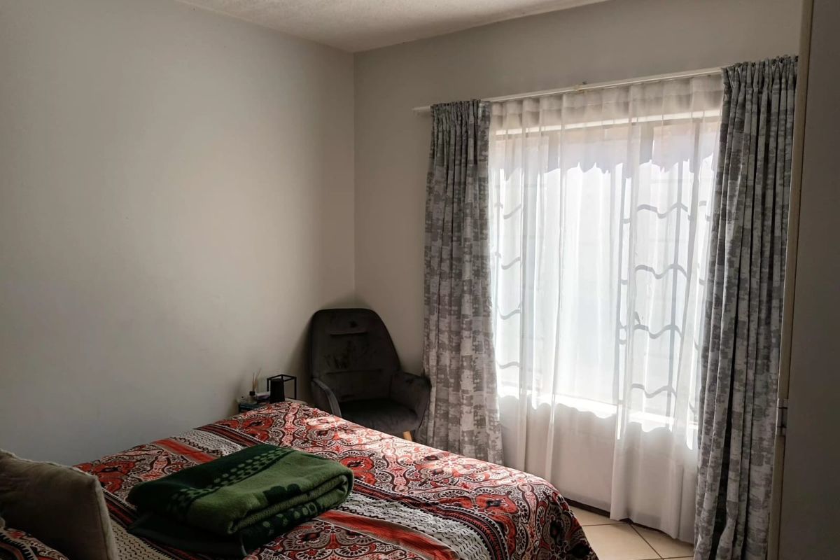 A bedroom featuring tiled flooring and natural light through a window with installed curtain tracks.