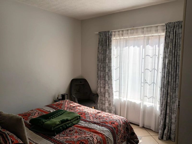 A bedroom featuring tiled flooring and natural light through a window with installed curtain tracks.