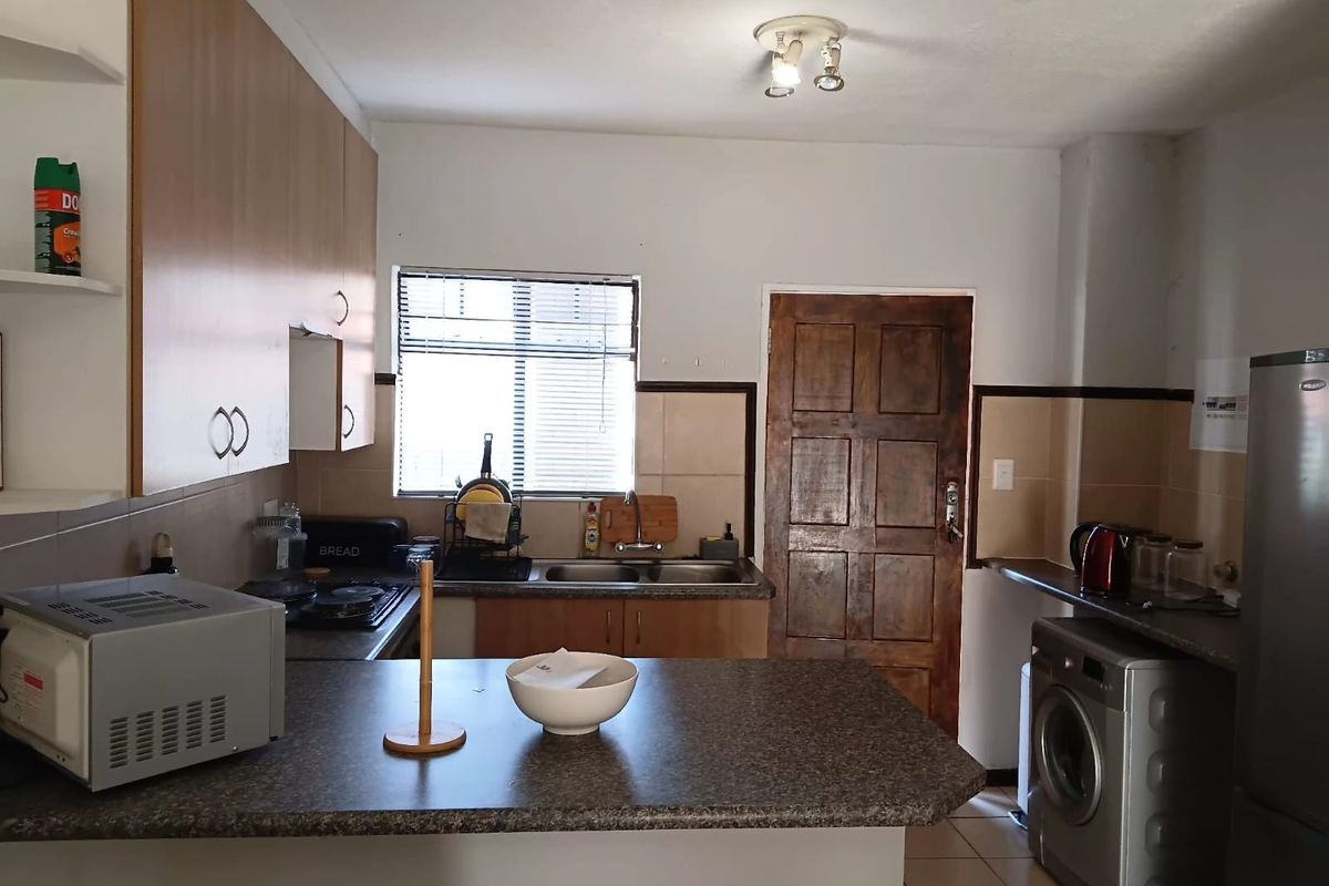 A functional kitchen featuring laminate cabinetry, laminate countertops, a double basin sink, and a built-in hob with tiled splashbacks.