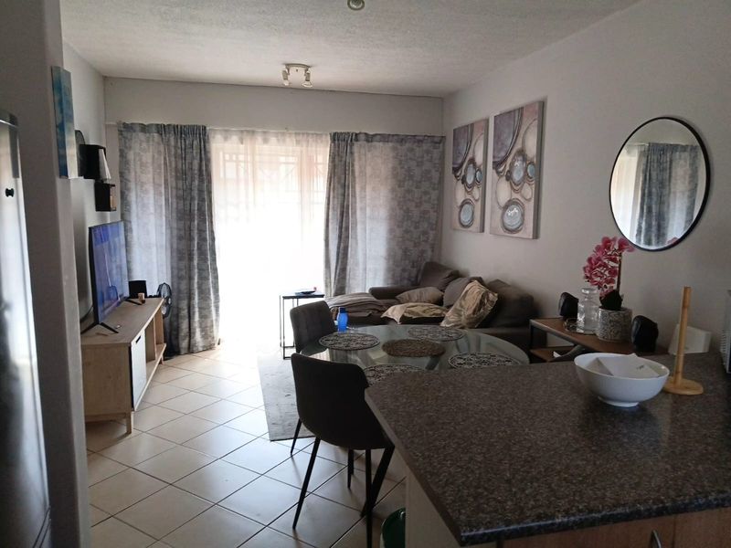 Open-plan living and dining area featuring tiled flooring, a granite kitchen breakfast bar, and access to a balcony through sliding glass doors.