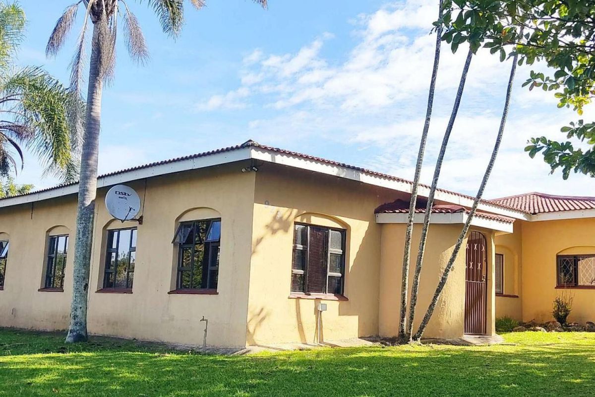 A view of the rear exterior of the house featuring a tiled roof, security gate, and established garden surroundings.