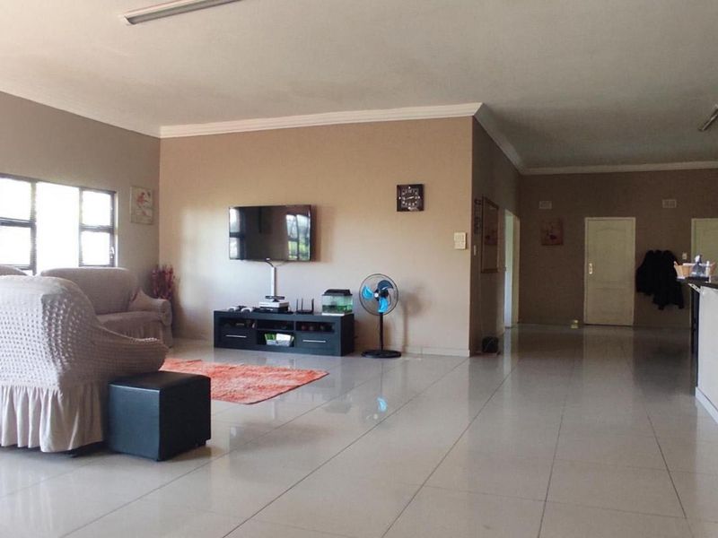 Spacious open-plan living area featuring neutral wall tones, tiled flooring, and a built-in breakfast bar, offering a versatile layout for modern living.