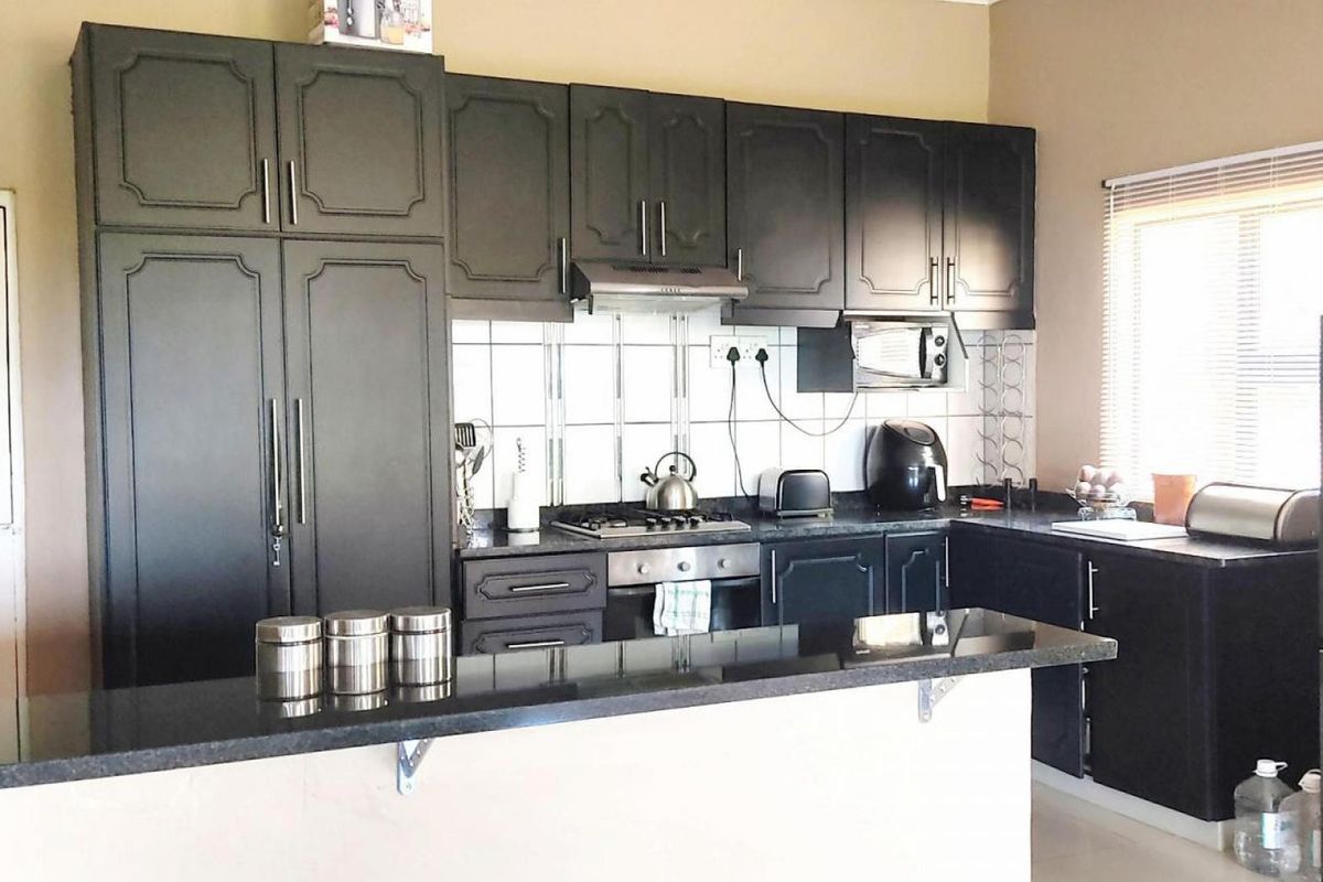 A functional kitchen featuring dark cabinetry, granite countertops, a breakfast bar, and a built-in gas hob with an extractor fan.