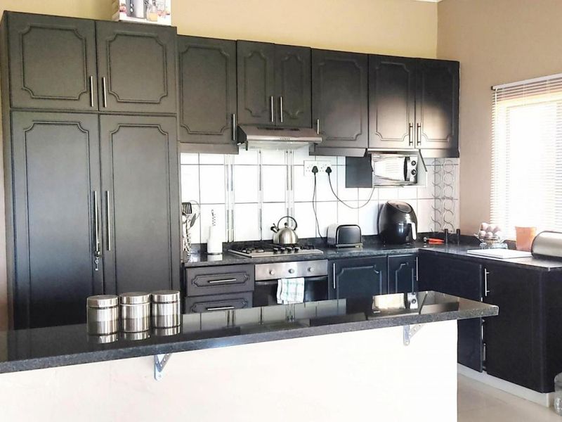 A functional kitchen featuring dark cabinetry, granite countertops, a breakfast bar, and a built-in gas hob with an extractor fan.