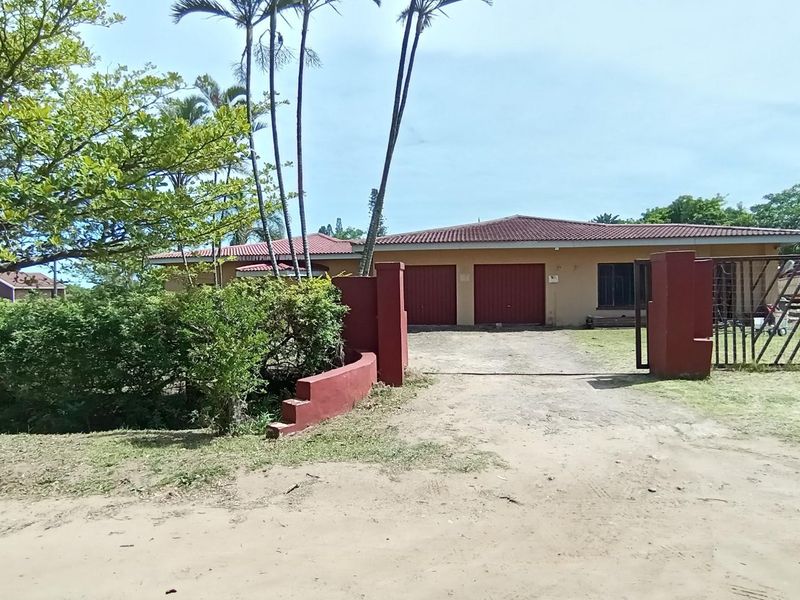 Front view of a single-story house featuring a double garage, gated entrance, and a large driveway set within a garden area.