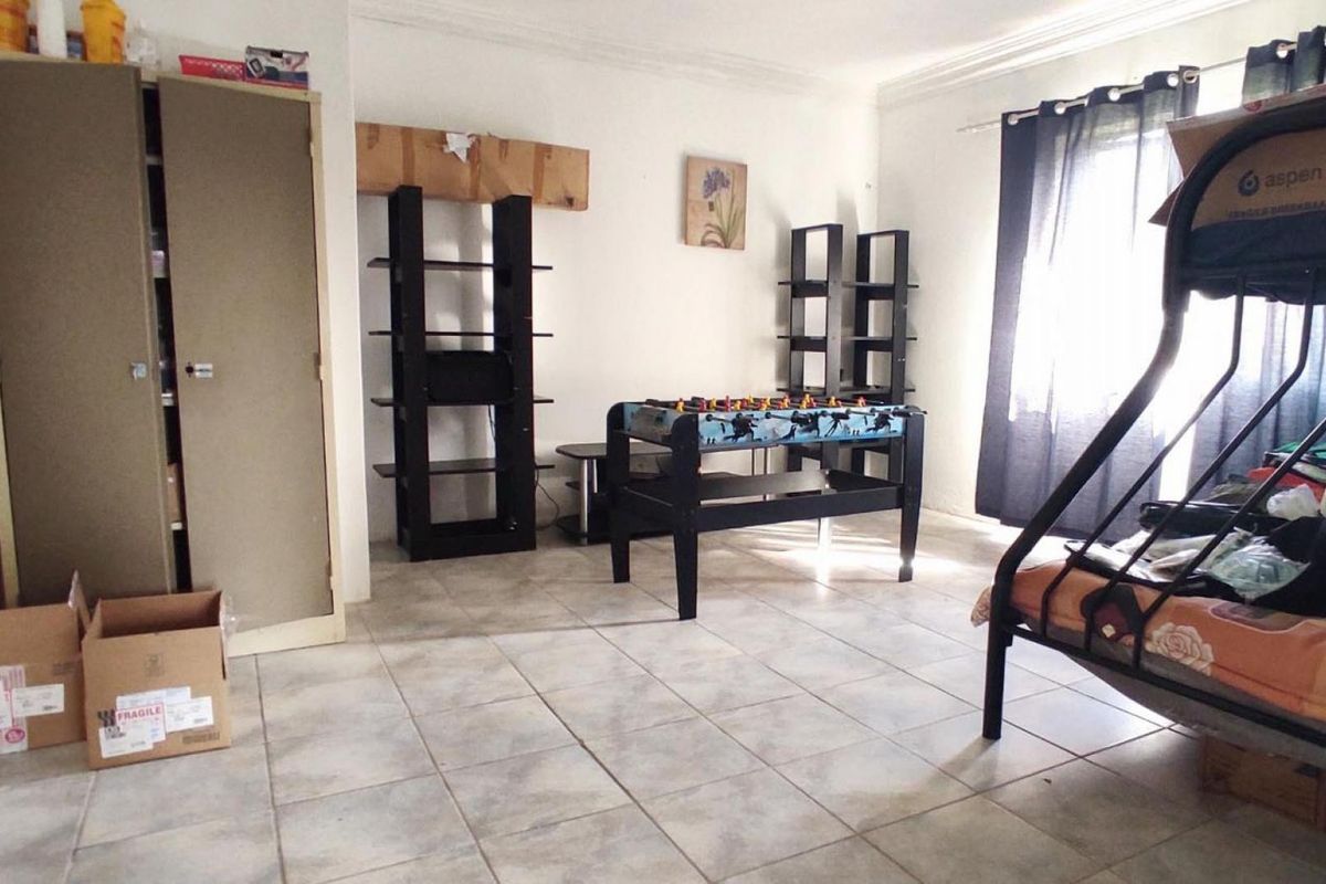 A bedroom featuring tiled flooring, a built-in cupboard, and cornice detailing, currently utilized as a multi-purpose living and sleeping space.
