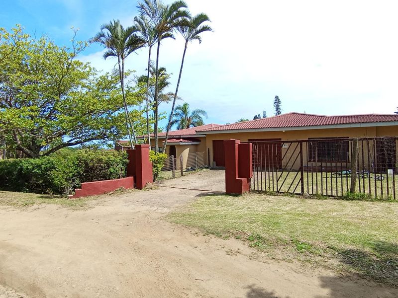 Front exterior view of a single-story house featuring a tiled roof, stucco facade, and a metal driveway gate with masonry pillars.