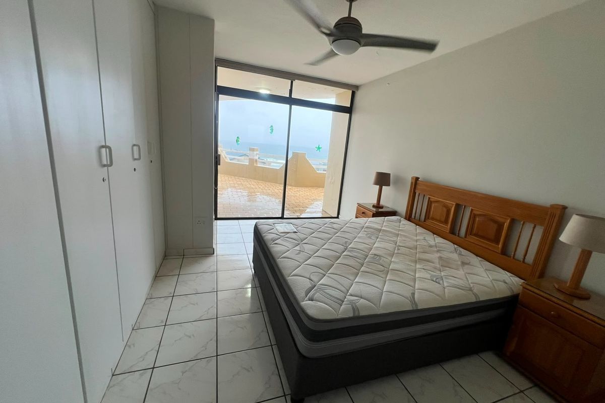 Bedroom featuring tiled flooring, built-in cupboards, a ceiling fan, and a sliding glass door providing access to a balcony with ocean views.