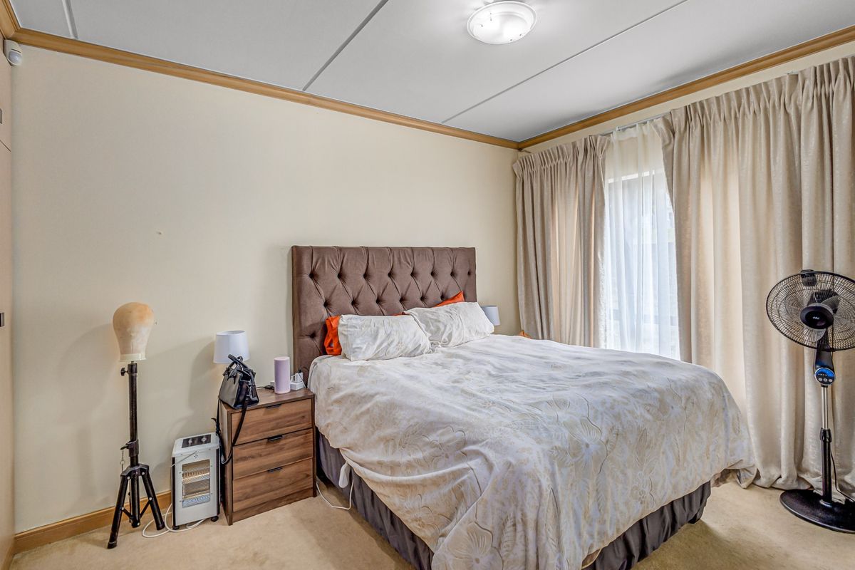 A standard bedroom featuring neutral walls, carpeted flooring, and a built-in cupboard with access to natural light through large window curtains.